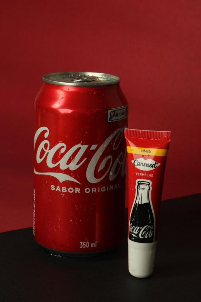 Lata de Coca-Cola junto al bálsamo labial Carmed