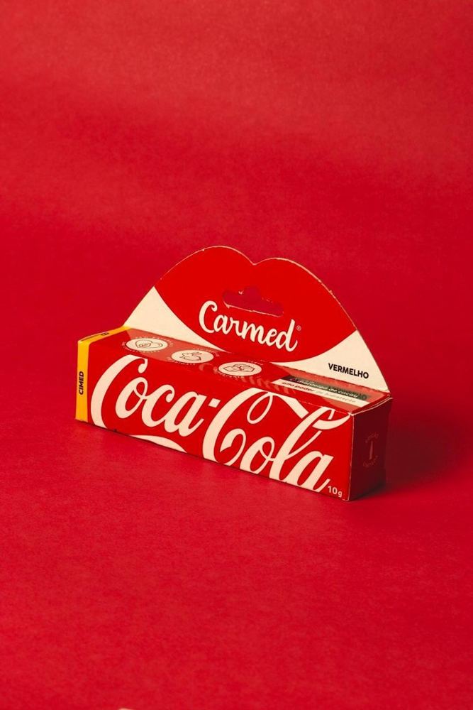 Bálsamo labial Carmed edición Coca-Cola en su caja, sobre fondo rojo