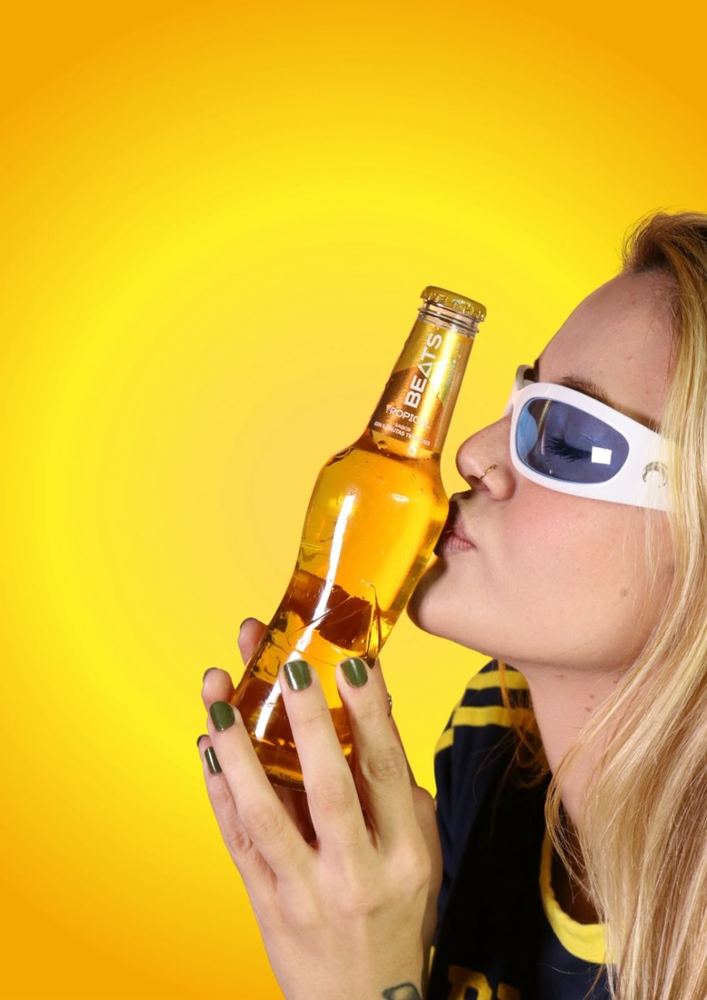 Modelo con una botella de Beats Tropical sobre fondo amarillo